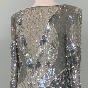 May include: A silver sequined dress with a geometric pattern. The dress has a long sleeve and a fitted silhouette.