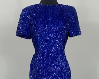 May include: A royal blue sequined dress with short sleeves and a fitted silhouette. The dress is on a mannequin.