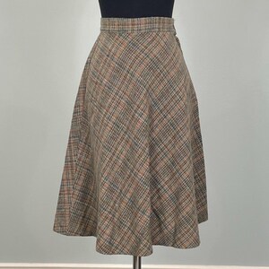 Peut inclure: Une jupe arrivant au genou avec un motif à carreaux marron, beige et bleu et une coupe en biais. La jupe présente une taille ajustée et une silhouette évasée qui tombe depuis la taille, révélant une texture tissée sur tout le tissu.