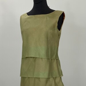 May include: A sleeveless, tiered dress in a light green colour. The dress is made of a silky fabric and has a simple, elegant design.