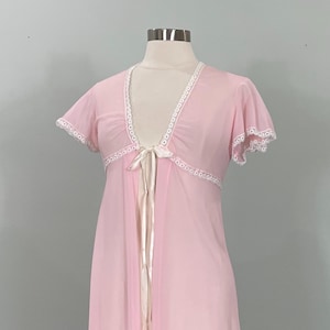 May include: A sheer, light pink robe with short sleeves and a tie closure. The robe features white lace trim along the edges and neckline. The garment is displayed on a mannequin.