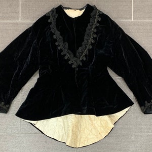 May include: A black velvet jacket with a lace trim around the collar, cuffs, and hem. The jacket has a fitted bodice and a flared skirt.