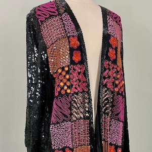 May include: A black sequined jacket with a patchwork design. The jacket features a variety of patterns in pink, orange, and copper sequins. The jacket is displayed on a mannequin.