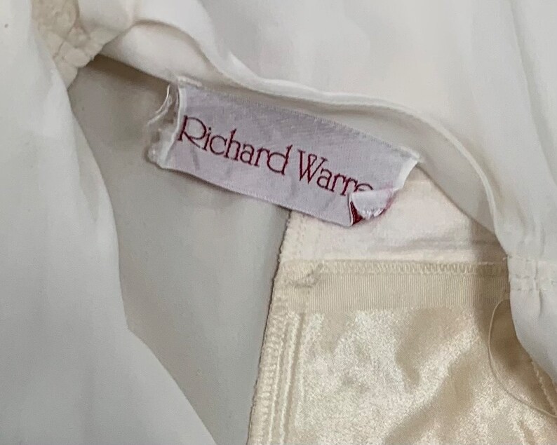 Może przedstawiać: Biały odzież z podszewką z białego satyny. Odzież ma etykietę z napisem "Richard Warren".