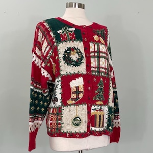May include: A red, green, and cream knit cardigan featuring a patchwork design of holiday motifs including a wreath, a stocking, a Christmas tree, and wrapped gifts. The button-front sweater has long sleeves with patterned bands and ribbed cuffs.