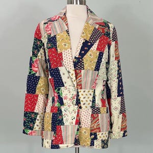 May include: A patchwork blazer with a vibrant mix of floral, paisley, and geometric patterns in red, navy, gold, and cream. The blazer features a classic notched collar, two buttons, and long sleeves. The jacket is displayed on a mannequin.