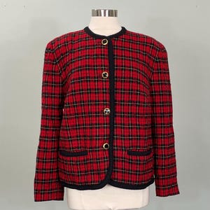 May include: A long-sleeved jacket featuring a red and black plaid pattern with a round neckline. The garment includes a dark navy blue braided trim along the edges, four gold-toned circular buttons down the front, and two front pockets.