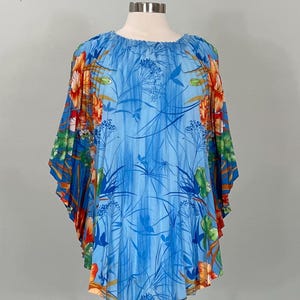 May include: A blue tunic top with a floral print. The top features a round neckline and wide sleeves. The floral pattern includes orange, red, and green flowers and foliage against a blue background.