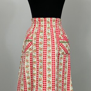 May include: A red and white gingham skirt with a floral print and a pink and green trim. The skirt has two pockets on the front.