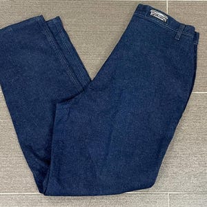 May include: Dark blue denim jeans. The jeans are folded and laid flat, showcasing the front and back. The brand name "ROCKY MOUNTAIN" is visible on the back waistband. The jeans have a classic five-pocket design and a straight leg cut.