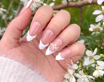 May include: Close-up of a hand with white french manicure nails with a white flower accent on one nail.