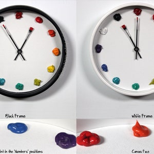 May include: Two wall clocks with black and white frames, featuring a white canvas face. Instead of numbers, dollops of colorful paint mark the hours. The clock hands are shaped like paintbrushes, with red bristles at the tips of the hands.