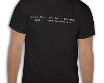 May include: Black t-shirt with white text: "If at first you don't succeed, call it beta version 1.0." The shirt is a crew neck style. The image shows the shirt on a person.