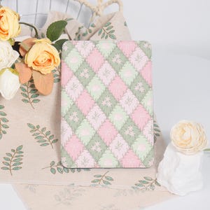 May include: An e-reader case with a pink and green geometric pattern. The case has a quilted look with a repeating design of small flowers and leaves.