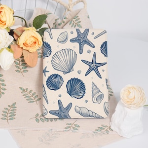May include: A rectangular, cream-colored notebook or journal featuring a repeating pattern of blue seashells and starfish. The design includes various shell shapes and sizes, creating a nautical theme. The cover is likely made of a durable material.