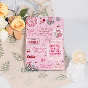 May include: Pink Kindle cover decorated with stickers. Stickers include text that says "I love my Kindle", "Bookish Baddie", "Pretty girls read books", and "Buy me books & tell me I'm pretty". Other stickers include cherries, bows, and disco balls.