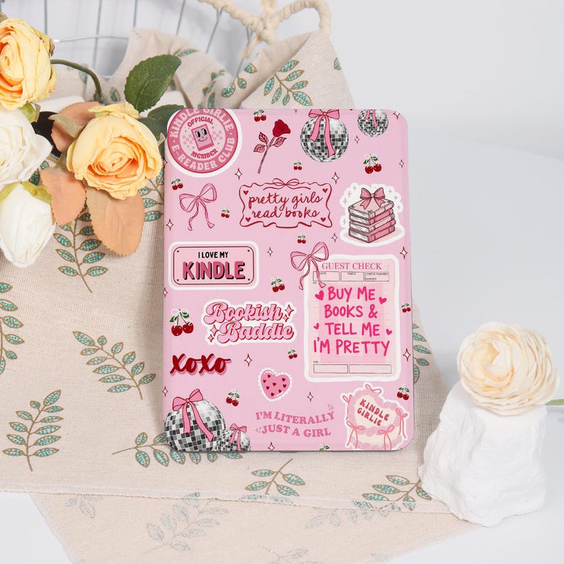 May include: A pink Kindle cover adorned with various stickers. The stickers feature phrases such as "I love my Kindle", "Bookish Baddie", and "Pretty girls read books". Other stickers include cherries, bows, and disco balls. The cover is decorated with a variety of cute designs.