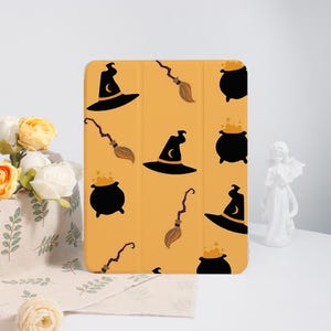 May include: A yellow tablet case featuring a repeating pattern of black witch hats with crescent moons, cauldrons, and brooms. The Halloween-themed design is set against a solid yellow background.