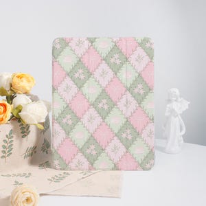 May include: A pink and green patterned iPad case with a quilted design. The pattern features small flowers, leaves, and bows.