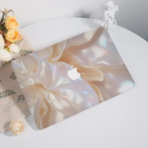May include: A white laptop skin with a pearlescent, iridescent, and abstract design. The skin features a subtle swirl pattern and a white Apple logo.
