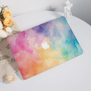 May include: A laptop case with a watercolour design in shades of pink, purple, yellow, and blue. The Apple logo is visible in white. The design gives an artistic and contemporary feel to the laptop.