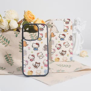 May include: Two phone cases with a repeating pattern of cartoon cats in various colors. The cases have a white background and a black border. One case is in focus, the other is slightly out of focus.