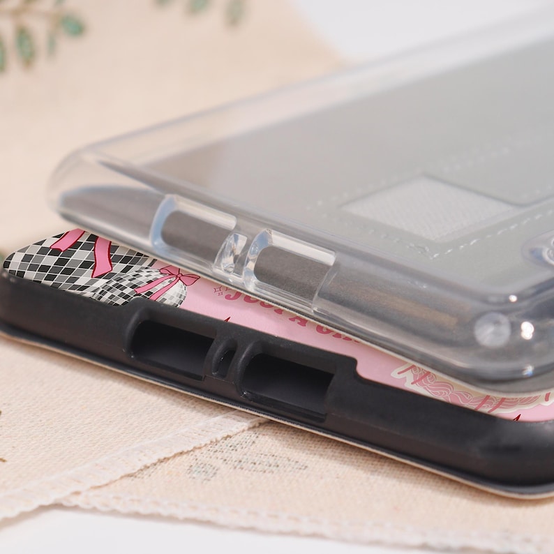 May include: Clear phone case stacked on top of a phone case with a black border. The bottom case has a pink and white design with a black and white checkered pattern and pink bows. The top case is transparent.