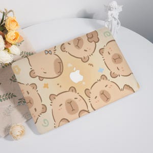 May include: A beige laptop skin with a repeating pattern of brown cartoon bears with a light brown background. The bears have a light brown nose and small black eyes. The skin has a white Apple logo in the center.