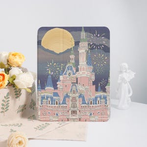 May include: A rectangular tablet case featuring a printed illustration of a pink and blue castle with tall spires against a dark purple night sky. A large yellow moon and white fireworks are visible above the castle structure.