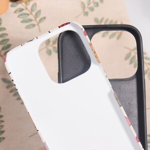 May include: White phone case with a colorful pattern and a black interior. The case has cutouts for the camera and buttons. The pattern includes red, pink, and brown elements. The case is designed to protect the phone.