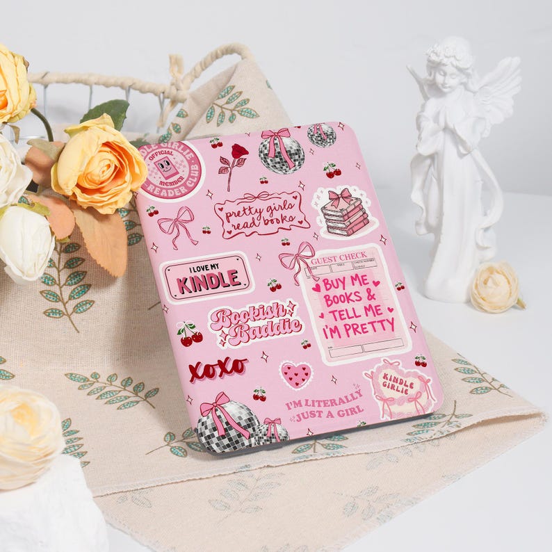 May include: A pink Kindle case adorned with various stickers. The stickers feature phrases like "I Love My Kindle" and "Pretty Girls Read Books," alongside bows, cherries, and disco ball motifs. The case is a stylish accessory.