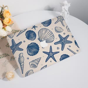 May include: A laptop case featuring a beige background with a pattern of blue seashells and starfish. The design includes various shell shapes and sizes, creating a nautical theme. The Apple logo is visible.