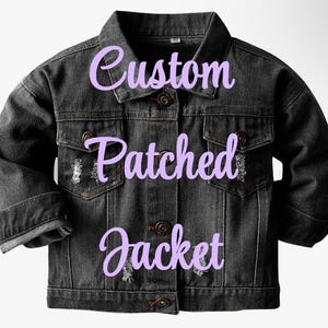 May include: A black denim jacket with a classic collar, button closure, and two chest pockets. The jacket has distressed details and the words "Custom Patched Jacket" in a light purple script.