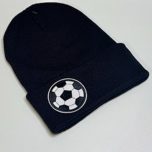May include: Black knit beanie with a soccer ball patch. The patch is a white and black soccer ball design. The beanie is a classic style, perfect for sports fans or anyone looking for a warm hat.