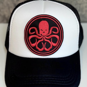 May include: Black and white trucker hat with a red octopus emblem on the front. The emblem is a red octopus design inside a black circle with a red border. The hat has a white front panel and a black mesh back.