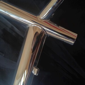 May include: Close-up of a polished chrome bicycle frame with welded joints. The frame is made of metal tubing and has a shiny, reflective surface.