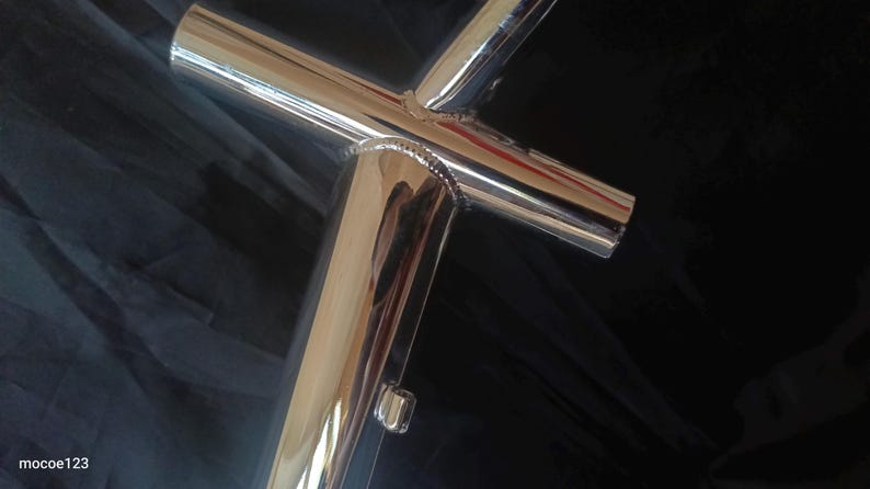 May include: Close-up of a polished chrome bicycle frame with welded joints. The frame is made of metal tubing and has a shiny, reflective surface.