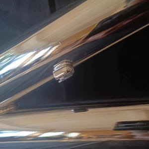 May include: Close-up of a chrome-plated metal surface with a small, silver-colored latch or lock. The surface is highly reflective, showing a reflection of the surrounding environment.