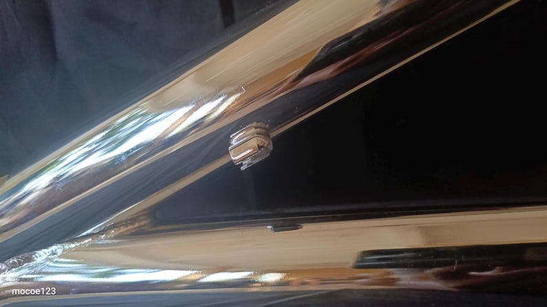 May include: Close-up of a chrome-plated metal surface with a small, silver-colored latch or lock. The surface is highly reflective, showing a reflection of the surrounding environment.