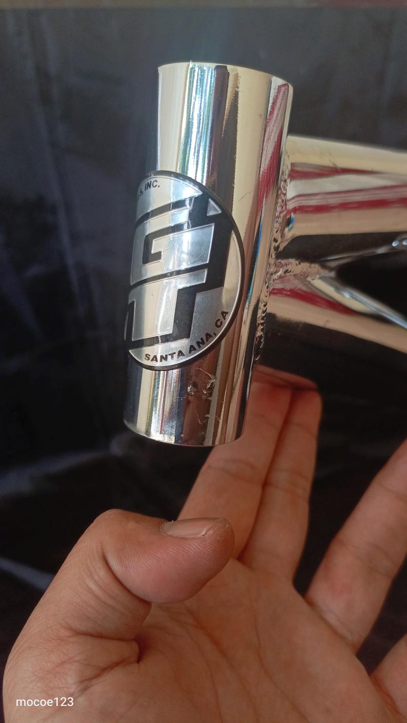 May include: Close-up of a chrome bicycle frame with a GT logo and the text "Santa Ana, CA" on a black background.