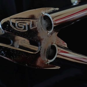 May include: Close-up of a chrome bicycle frame with the word "GT" embossed on the top tube.
