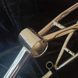 May include: A chrome bicycle frame with a round, hollow tube on the front. The frame is made of metal and has a shiny finish.