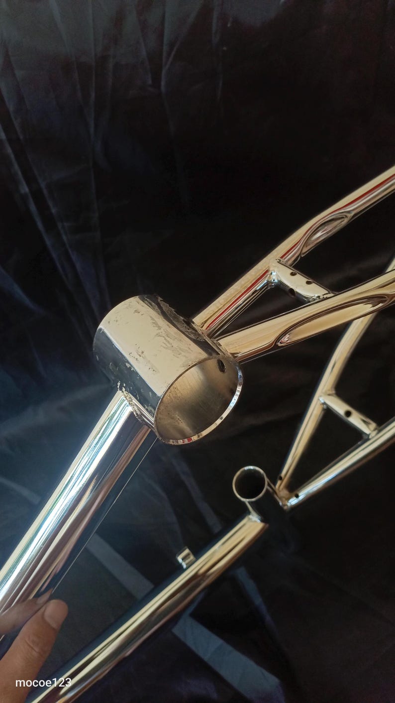 May include: A chrome bicycle frame with a round, hollow tube on the front. The frame is made of metal and has a shiny finish.