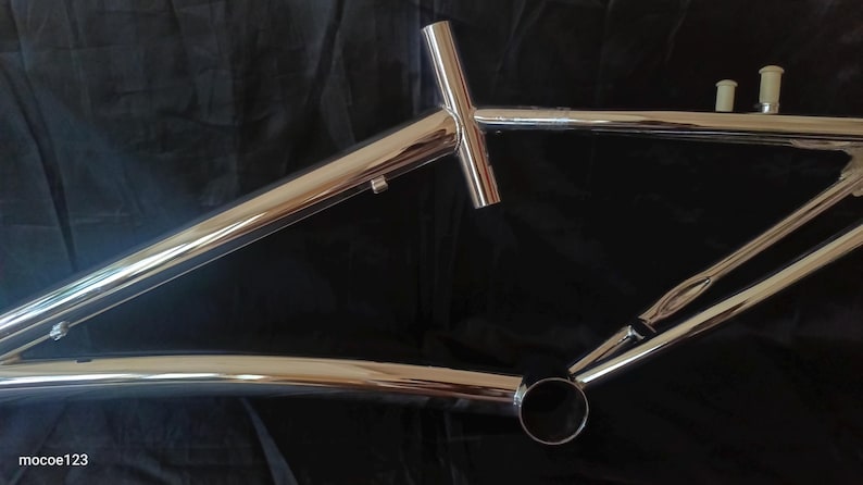 May include: A chrome bicycle frame with a T-shaped top tube and a rear dropout. The frame is on a black background.
