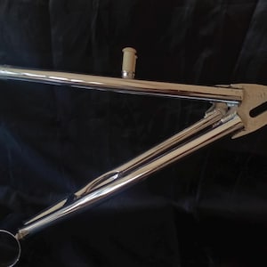May include: Chrome bicycle frame with a silver finish. The frame has a curved top tube and a straight down tube. The frame is designed for a BMX bike.
