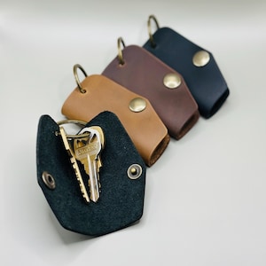 May include: A collection of leather keychains in various colors: black, brown, tan, and dark brown. Each keychain features a metal snap closure and a metal ring for attaching keys. One keychain is open, displaying several keys.