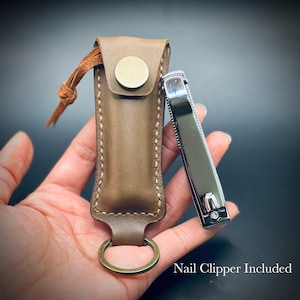 May include: A brown leather nail clipper case with a brass button closure and key ring. A silver nail clipper is included. The case is hand-stitched and has a leather cord detail.