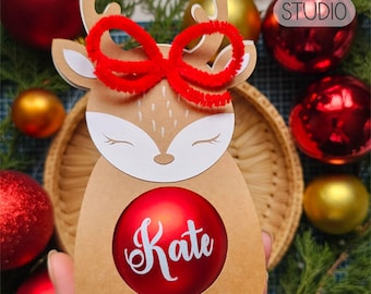 May include: A brown paper reindeer ornament holder with a red bow and a red ornament that says "Kate" inside. The ornament holder is 5.5 to 6 cm (2.16 to 2.36 inches) in diameter.