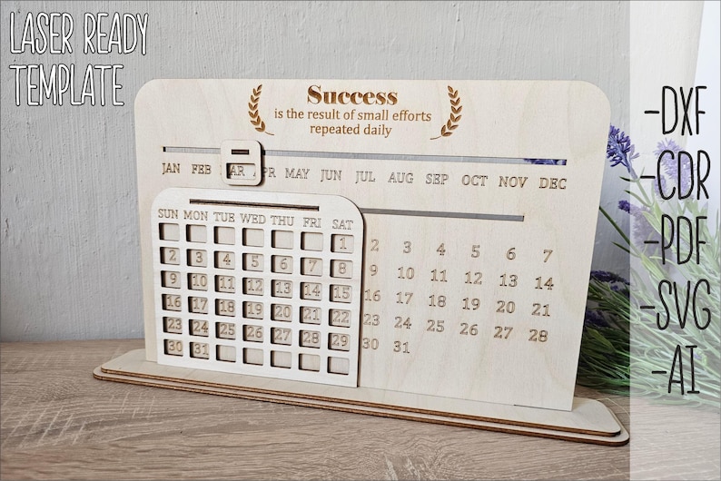 K&ouml;nnte beinhalten: Ein lasergeschnittener Holz-Desktop-Kalender mit einem monatlichen Kalenderrraster und einem Zitat &uuml;ber Erfolg. Das Zitat lautet "Erfolg ist das Ergebnis kleiner Anstrengungen, die t&auml;glich wiederholt werden".