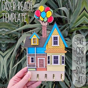 May include: Laser cut template of a colourful house with balloons on top, designed to be used as a key holder. The house is blue, yellow, and brown with a red door. The balloons are red, yellow, green, and blue. The template is available in DXF, CDR, PDF, SVG, and AI formats.  LASER READY TEMPLATE